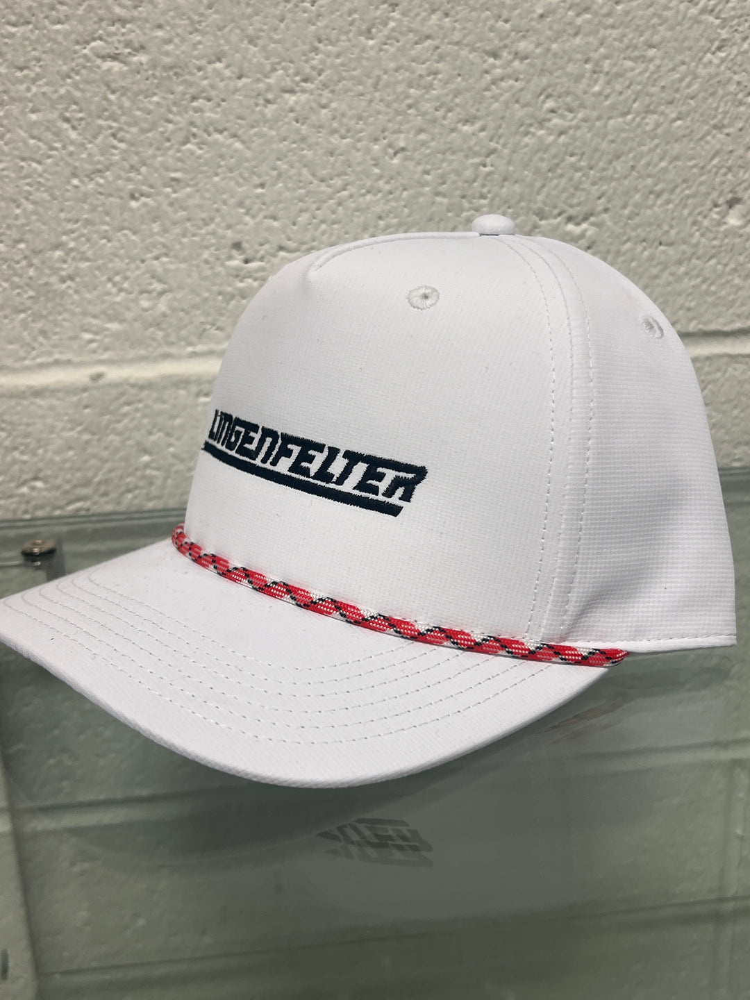 White cap with red brim and black logo against a gray wall
