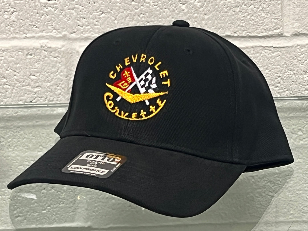 A black baseball cap featuring an embroidered Chevrolet Corvette logo on the front and an OTTO brand sticker on the brim, set against a white brick wall background.