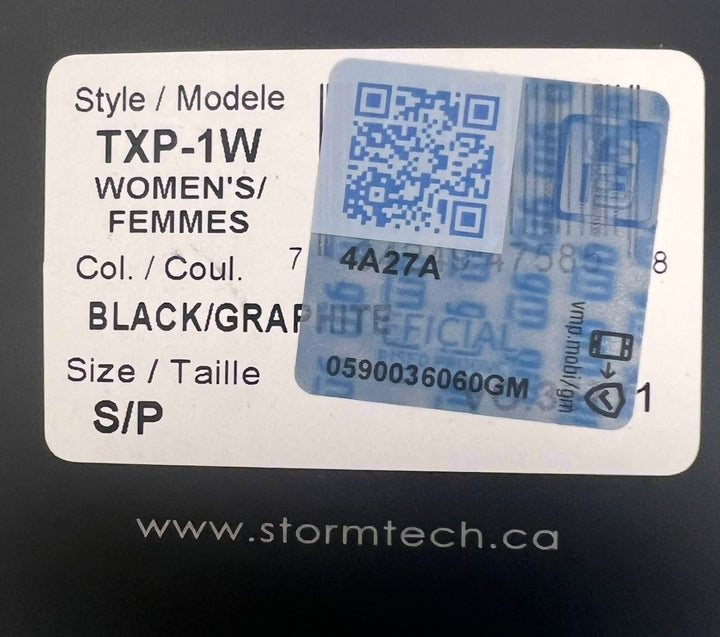 A close-up of a product label sticker on a black surface. The white label shows text including 'Style / Modele TXP-1W', 'WOMEN'S/ FEMMES', 'Col.