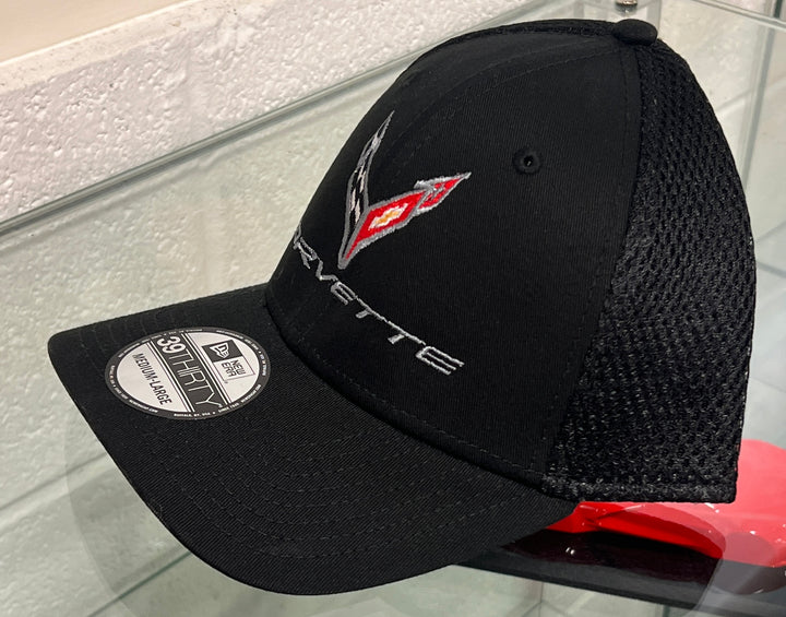 A black New Era 39FIFTY trucker cap featuring a Corvette logo embroidered on the front, displayed on a glass surface.