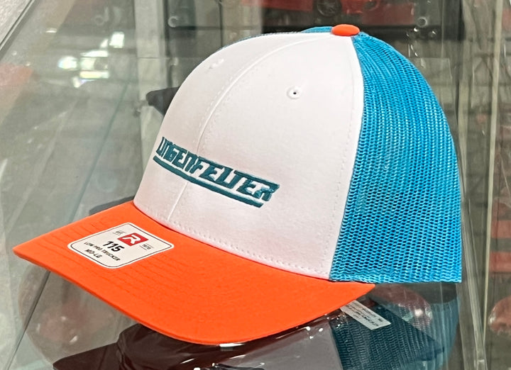 A trucker-style baseball cap with a white front panel, light blue mesh back panels, and an orange visor. The front panel features the brand name 'UNIDEFWEITER' in teal lettering with a white outline.