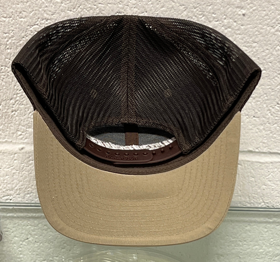 A trucker-style baseball cap viewed from the back, featuring a beige flat brim and a dark brown mesh back. The brand name 'Grunt Style' is embossed on the brown leather underband.