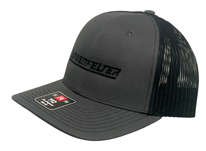 A dark gray and black trucker cap with a structured dark gray front panel and bill, black mesh back, and a black embroidered 'MUNGENFELTER' logo on the front. A size sticker is visible on the brim.