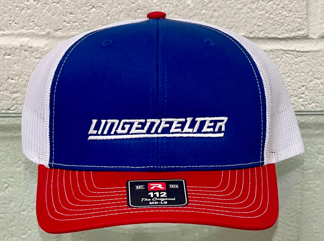 A red, white, and blue trucker-style cap with 'LINGENFELTER' embroidered in white across the blue front panel. The cap features a blue front, white mesh back panels, and a red brim, shown against a light gray brick wall background.