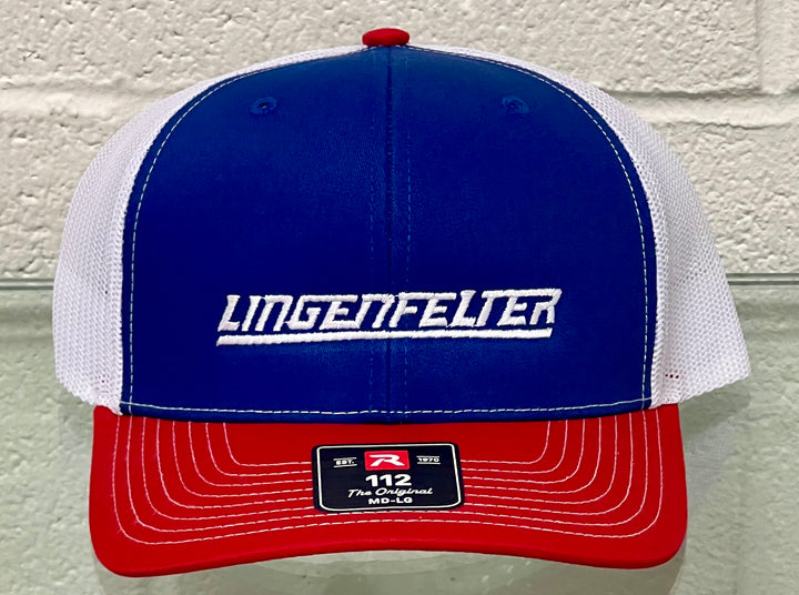 A red, white, and blue trucker-style cap with 'LINGENFELTER' embroidered in white across the blue front panel. The cap features a blue front, white mesh back panels, and a red brim, shown against a light gray brick wall background.