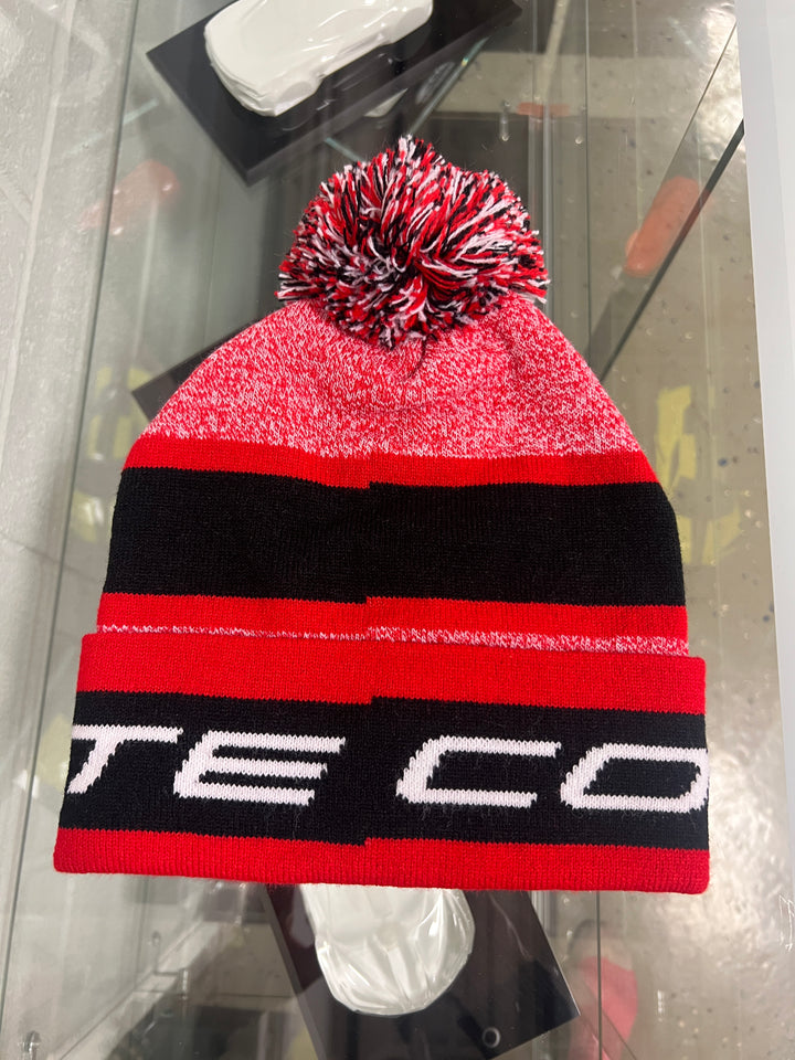 Red and black knit beanie with a pom-pom on a reflective surface