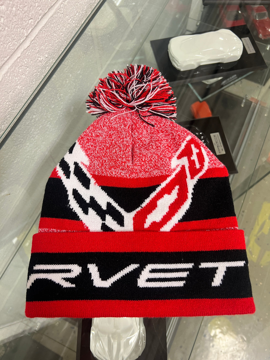 Red, black, and white beanie with pom-pom on a car's rearview mirror