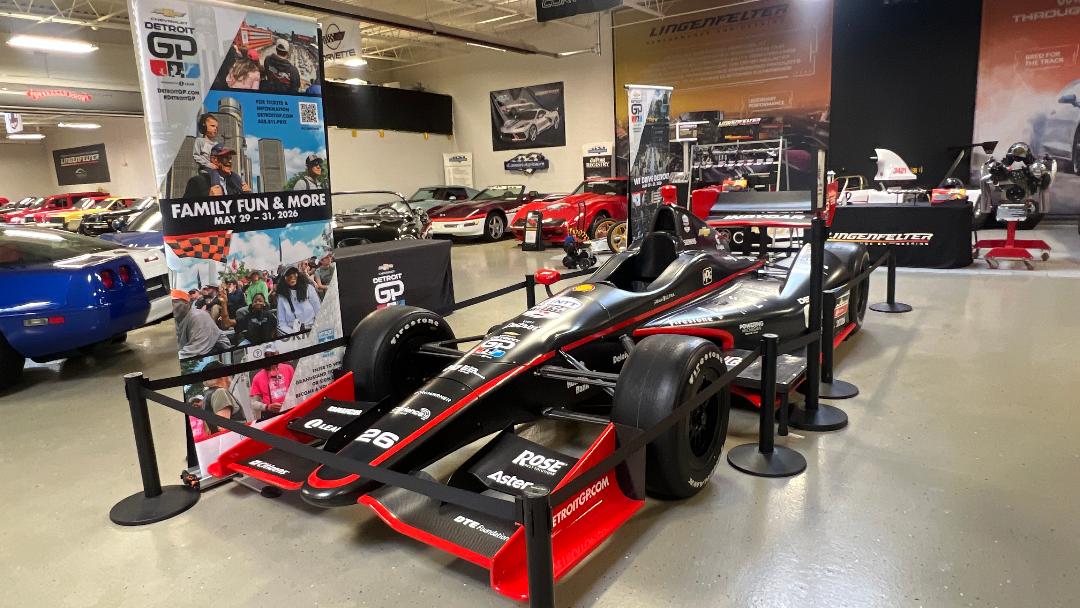 Formula 1 car on display in a showroom with promotional banners and other vehicles in the background.