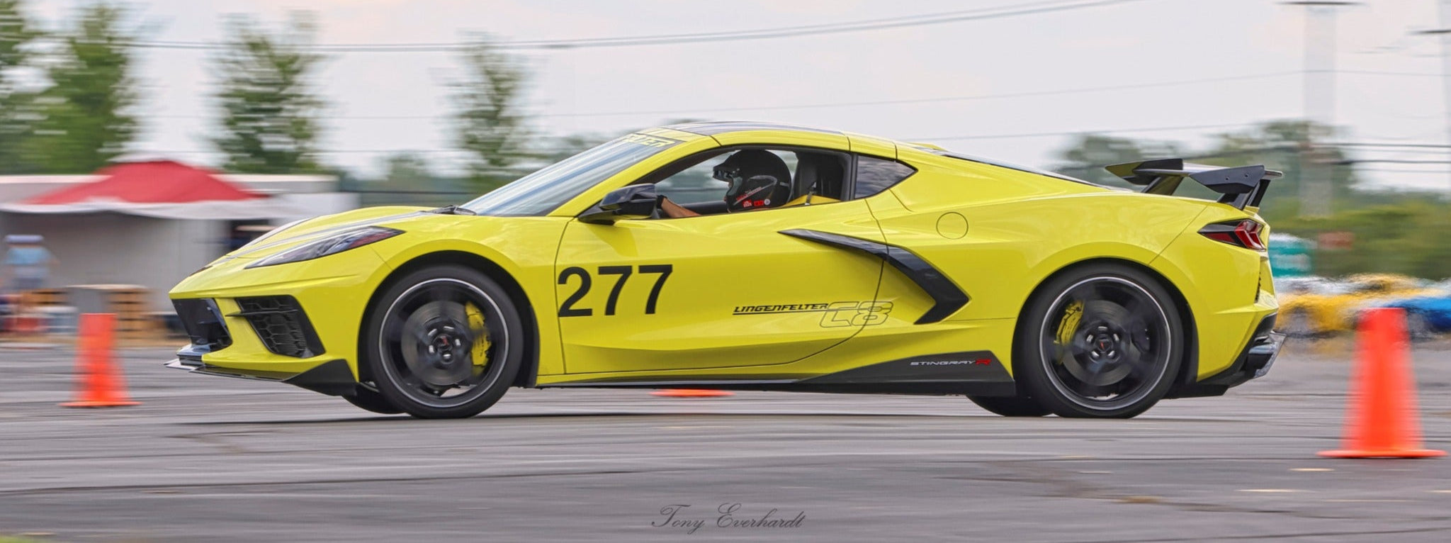 Yellow sports car with the number 277 on a track with orange cones and a blurred background.