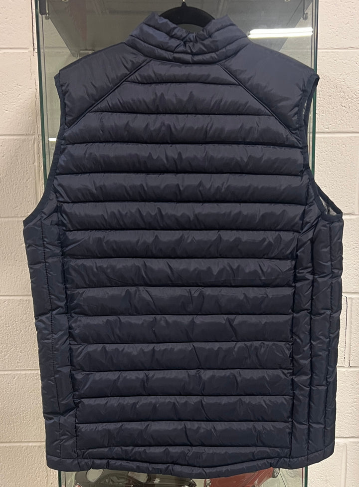 A navy blue sleeveless puffer vest with horizontal quilting, shown hanging on a black hanger against a light gray brick wall.