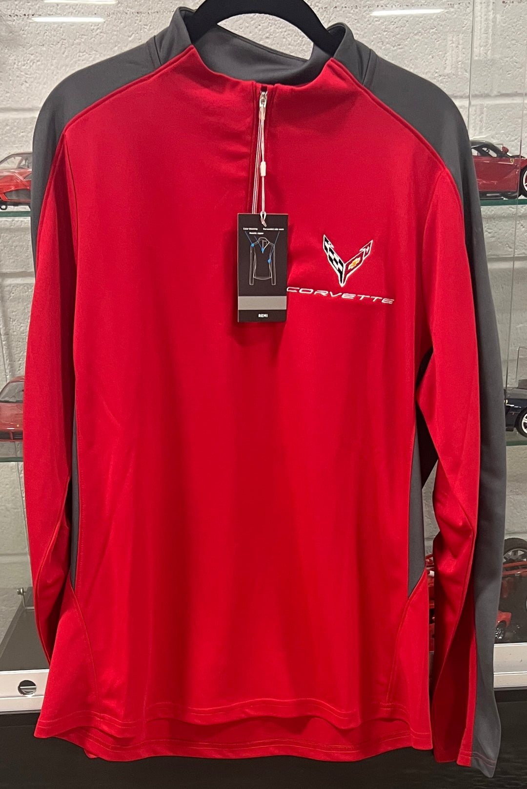 A red and gray long-sleeve quarter-zip athletic pullover with a Corvette logo on the left chest, hanging on a black hanger with a product tag attached.