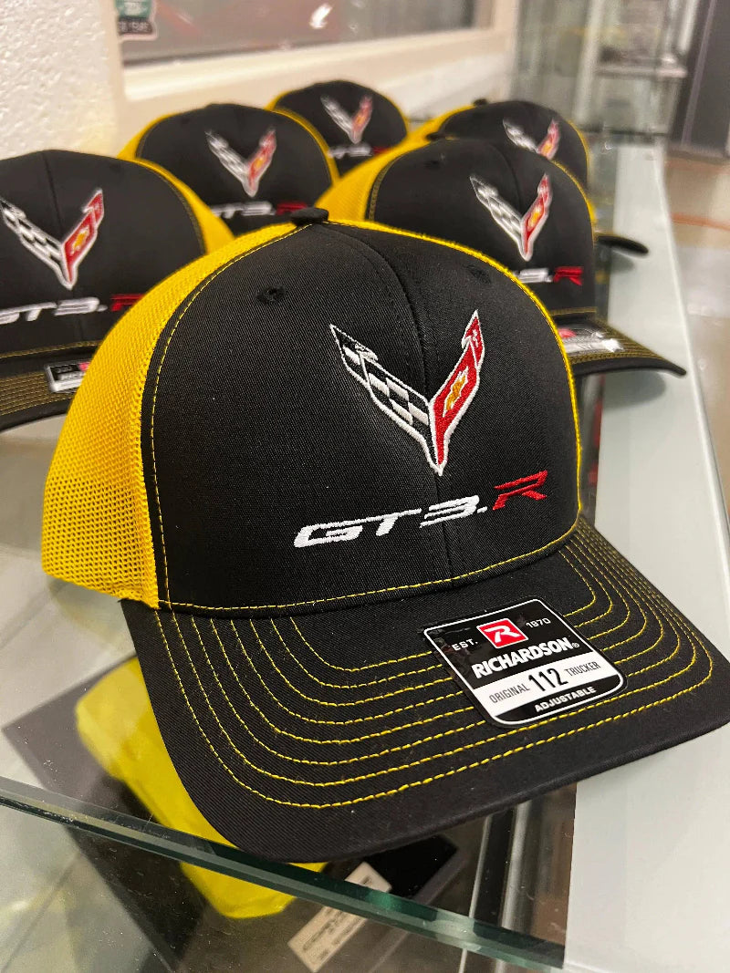 Black and yellow cap with GT3.R branding on a glass display table.