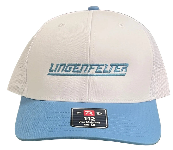 A white and light blue trucker-style cap with 'UMGENFELTER' embroidered on the front, displayed on a glass shelf.