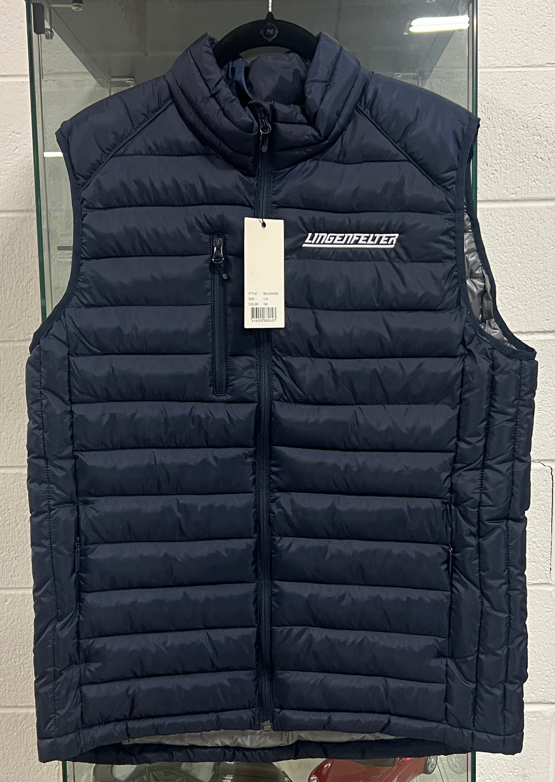 A navy blue puffer vest from Uniqlo's Line Store, hanging on a black hanger against a glass display case. The vest features a high collar, a front zipper, a vertical zip pocket, and a white 'UNIQLO LINE STORE' logo on the chest.